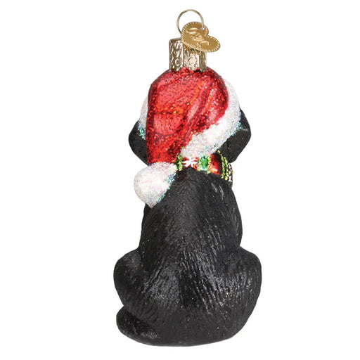 The Holiday Black Labrador Puppy Old World Christmas Ornament 12638 features a charming black Labrador puppy looking away, adorned with a sparkling red Santa hat and a joyful collar. It includes a golden loop on top for easy hanging on the tree.