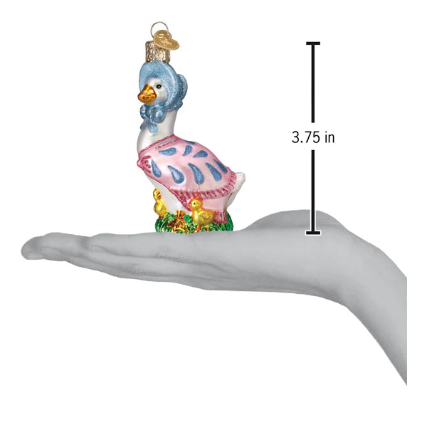 A hand holds a Jemima Puddle-Duck Old World Christmas glass ornament, measuring 3.75 inches tall. The ornament features Jemima adorned in a blue bonnet and pink shawl, standing on grass with two tiny yellow chicks at her side, perfectly capturing the quaint charm of a farmyard duck scene.