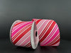 Two spools of 2.5X10Y Red Glitter-Fuchsia-Pink-White Diagonal Stripe Satin Ribbon are set on a dark surface, one tilted to display the vibrant pattern. The wired edges help your designs maintain their shape beautifully.