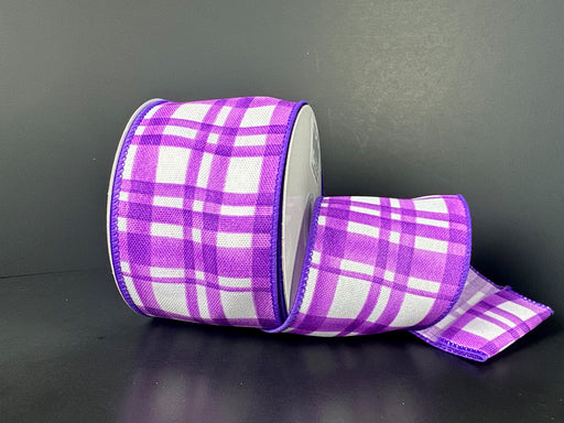 The 2.5X10Y Purple Watercolor Tuttola Plaid Ribbon 41546-40-11 is partially unrolled on a dark surface, showcasing its design.