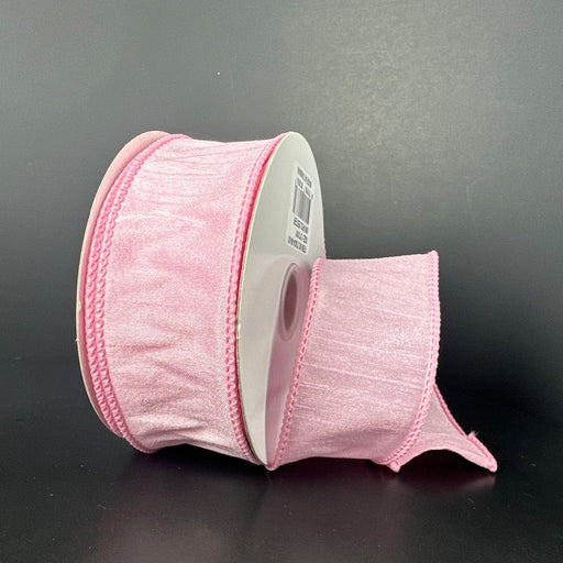 A spool of 1.5X10Y Pink Faux Dupioni Ribbon 72434-09-03, featuring a textured surface and decorative edges, is partially unrolled on a black surface against a dark background.