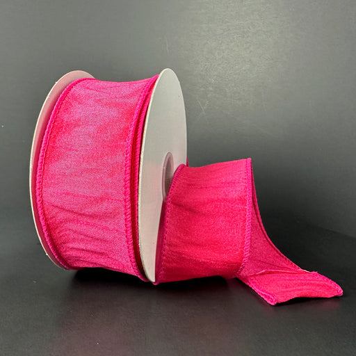 A spool of 1.5X10Y Fuchsia Faux Dupioni Ribbon sits unrolled against a dark background, showcasing its wired, shimmery texture that captures the light beautifully.