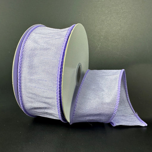 The 1.5X10Y Lavender Faux Dupioni Ribbon (72434-09-30) is partially unrolled, featuring neatly stitched wired edges for easy shaping, with a subtle sheen that stands out against the solid dark background, highlighting its delicate texture and soft hue.