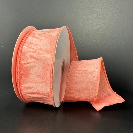 A spool of 1.5X10Y Coral Faux Dupioni Ribbon 72434-09-46 is set against a dark background, partially unrolled to highlight its wide, wired design with texture and sheen.