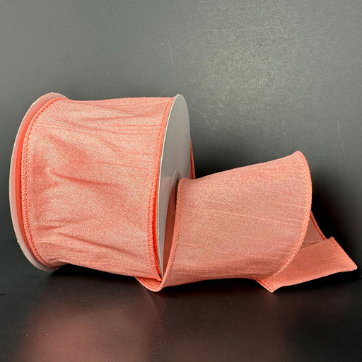 A 2.5X10Y Coral Faux Dupioni Ribbon (72434-40-46) shimmers on a black background, its wired texture partially unrolled to create an elegant curve.