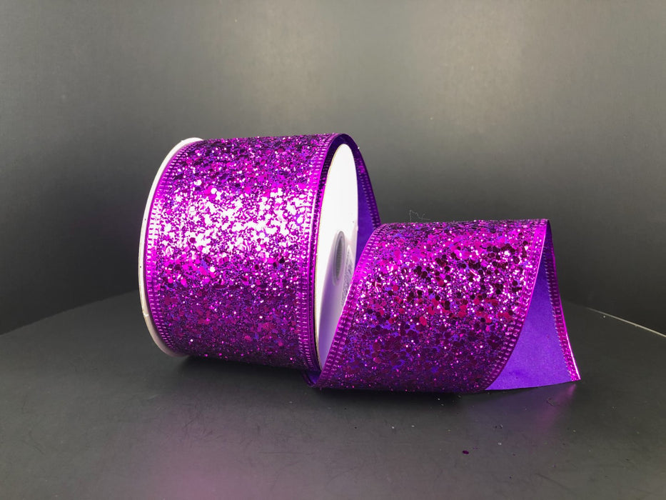 A partially unrolled spool of the 2.5"X10Y Purple Super Glitter Ribbon 75102-40-11 is set against a dark gray background, with the ribbon glistening under the light to highlight its shimmering texture.