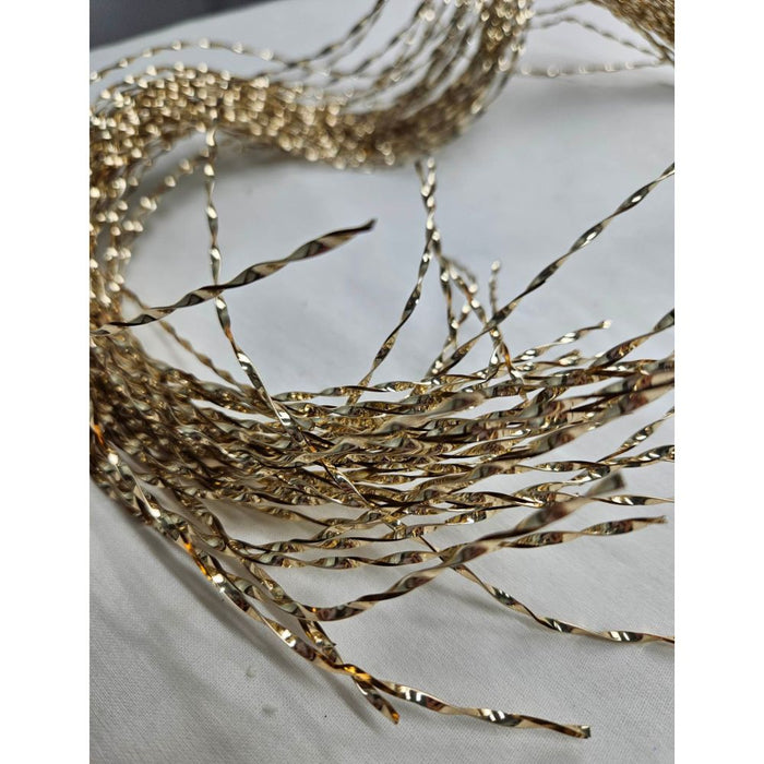 A close-up of numerous strands of thin, twisted golden wires arranged on a white surface showcases their shimmering gold metallic stripes, intricately intertwined to create a shiny and reflective texture reminiscent of the elegance found in the 39" Gold Metallic Stripe Hanging 82315-Gold design.