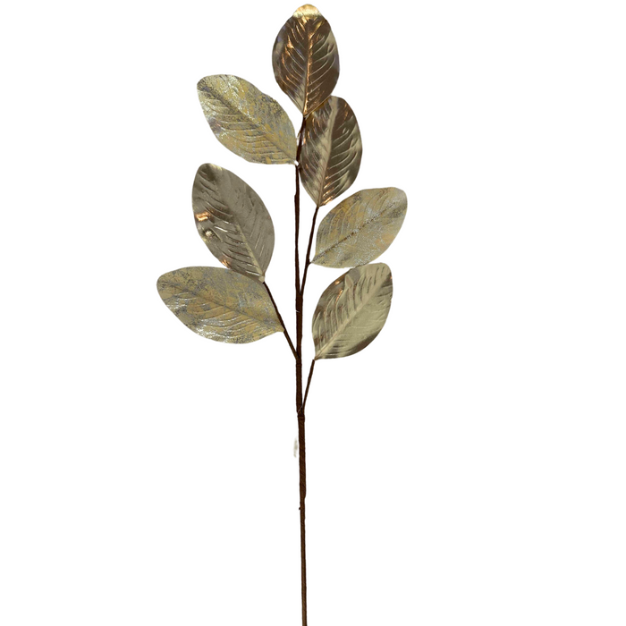 Introducing the 27" Champagne Metallic Magnolia Leaves Spray ISB78100, showcasing decorative magnolia leaves with a metallic finish in a champagne hue, artfully arranged along a central branch on a pristine white background. The spray's shiny, reflective surfaces add an extra touch of elegance and allure.