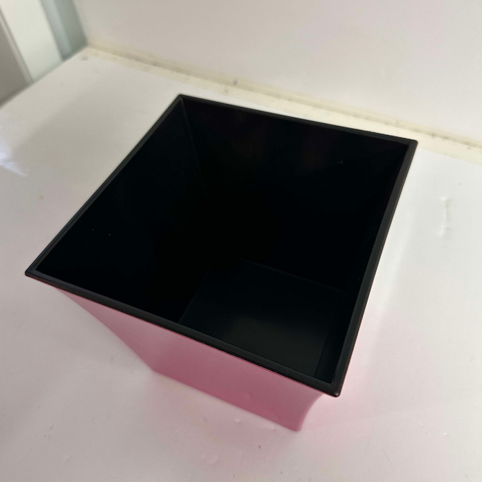 A 6" Hot Pink Square Plastic Pot P021516HP, featuring a black lining, sits empty on a white surface and is viewed from above.