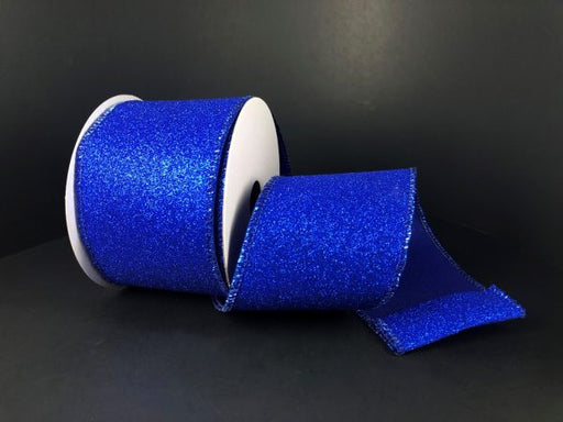 The 2.5X10Y Royal Blue All Flat Glitter Ribbon X820640-25 is partially unrolled against a dark background, its glittery surface catching the light.