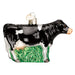 This hand-painted glass ornament, known as the Black Dairy Cow Ornament from Old World Christmas (12659), showcases a black and white dairy cow standing on a vibrant patch of green grass. It comes with a small gold cap and a heart-shaped tag on top for easy hanging, making it an ideal addition to your holiday decor.