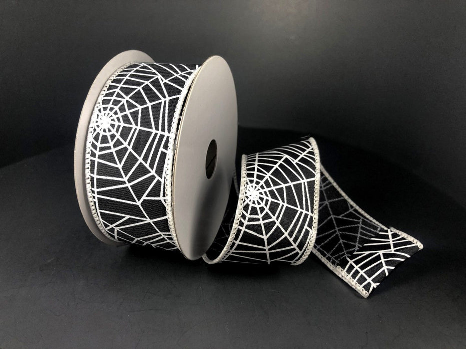 A partially unrolled roll of Black Satin/Spider Webs ribbon (1.5X10Y, 51007-09-21) rests against a dark background.