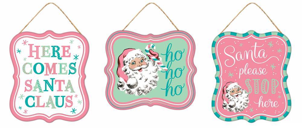 This set of Santa holiday decor, named "Three 7"Hx6"L Tin Matte Santa Signs White/Pink/Green/Teal MD1213A7," showcases vibrant designs. One sign reads "Here Comes Santa Claus" in colorful letters, another features Santa's face with a cheerful "ho ho ho," and the third charmingly requests, "Santa, please stop here," bordered in pink and teal.